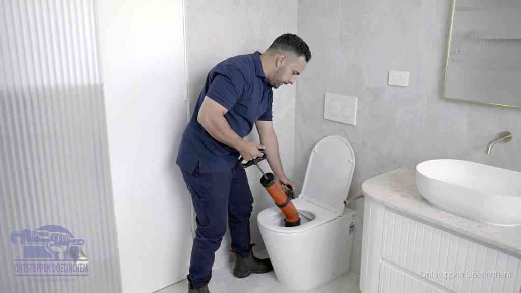 Een monteur buigt over een wandcloset en duwt met de hand een persluchtontstopper in de toiletpot om de verstopping handmatig los te maken in Doetinchem