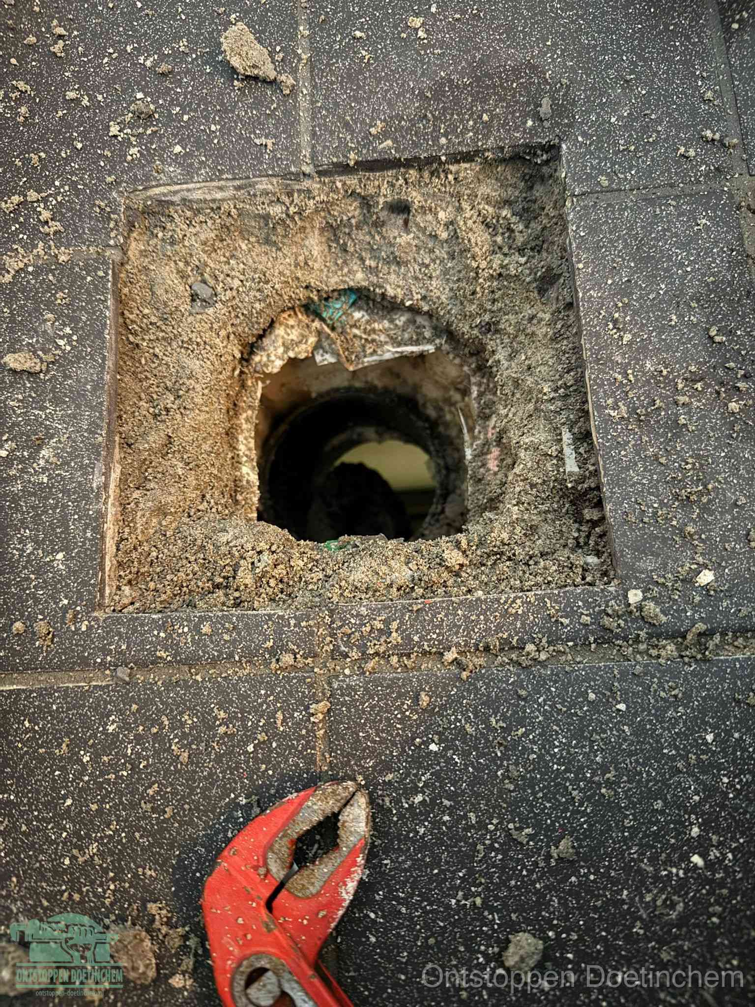 Een geopend rioolputje in een betontegelvloer met losgemaakt rooster en een zichtbare ronde afvoerbuis, het achterhalen waar de afvoerverstopping zit in Doetinchem