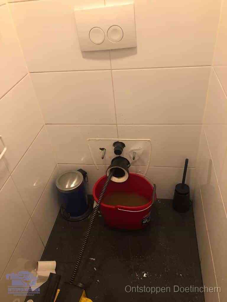 Een ontstopte wand-wc met verwijderde toiletpot waar een ontstoppingsveer in de wanduitgang verdwijnt, het achterhalen waar de verstopping zit in Doetinchem