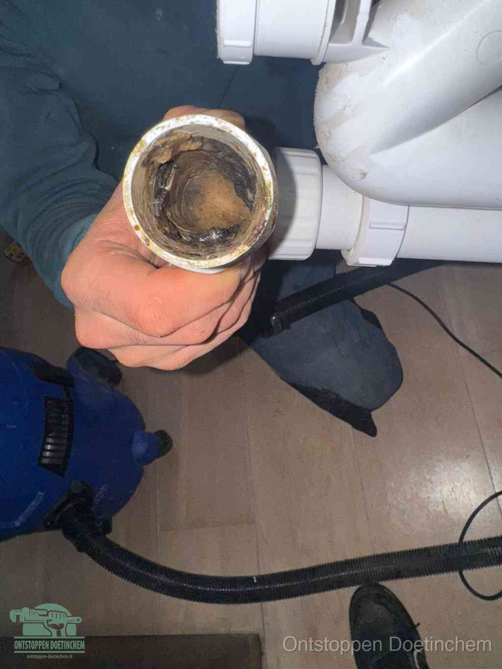 Een hand houdt een losgekoppeld PVC-afvoerbuisstuk vast dat van binnen volledig is dichtgeslibd met vet, vuil en aanslag, de meest voorkomende oorzaak van een verstopte afvoer in Doetinchem