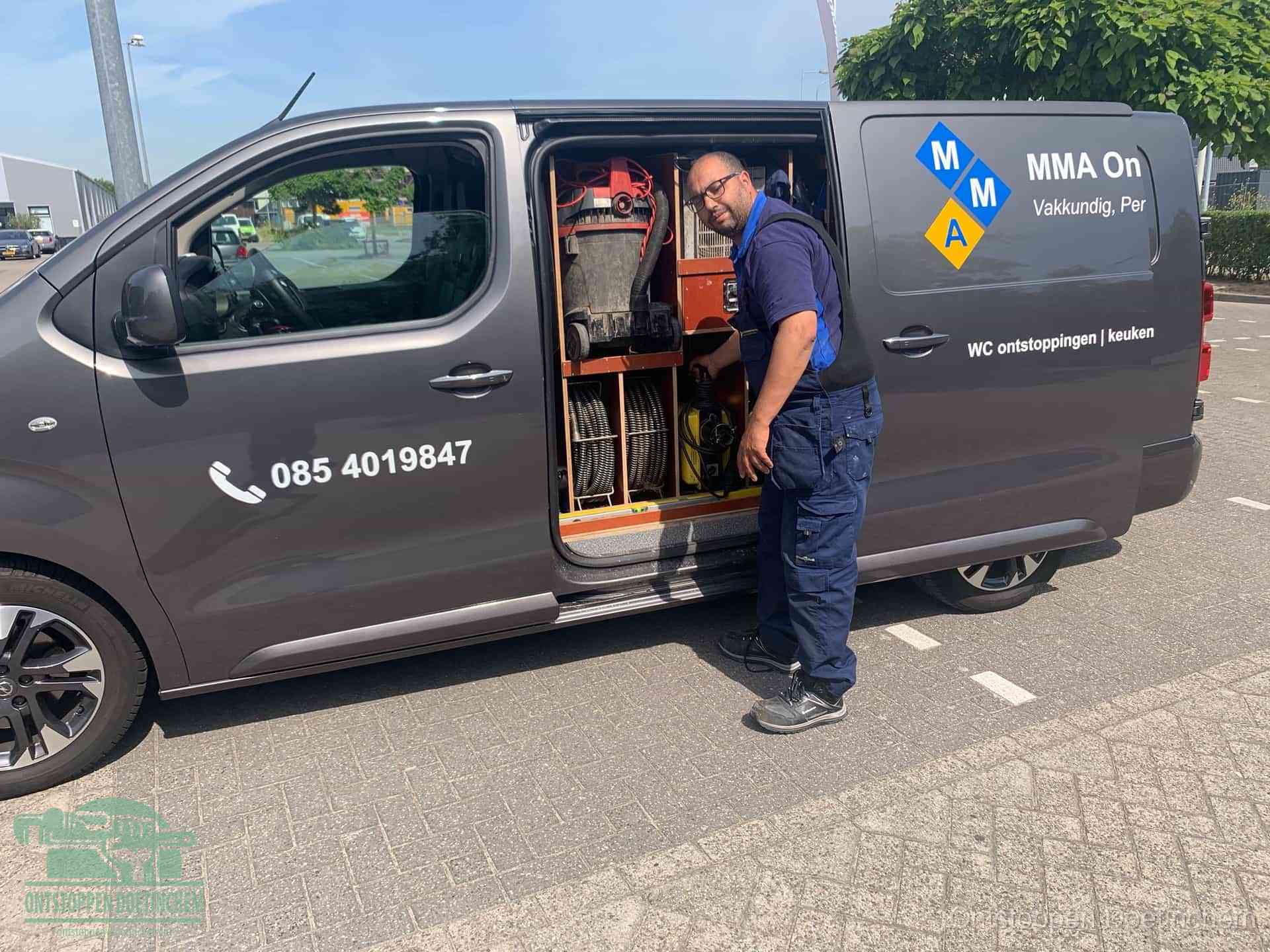 Een monteur bij de open schuifdeur van zijn bedrijfsbus op een parkeerplaats, klaar om de oorzaak van terugkerende afvoerverstoppingen aan te pakken in Doetinchem
