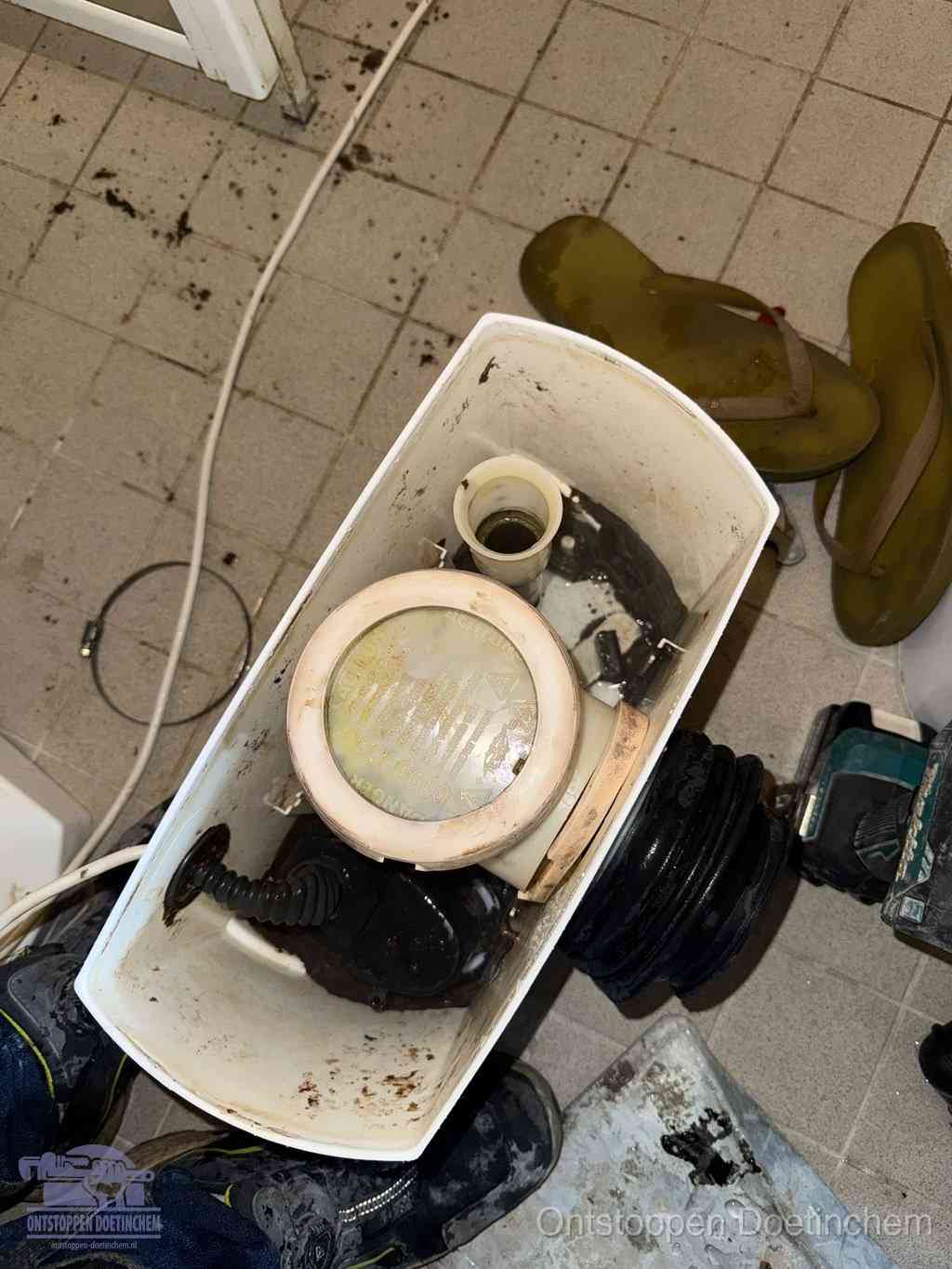 Een gedemonteerde toiletpot op de vloer met ontstoppingsveer en gereedschap ernaast, het verwijderen van een vastzittend voorwerp uit de wc in Doetinchem