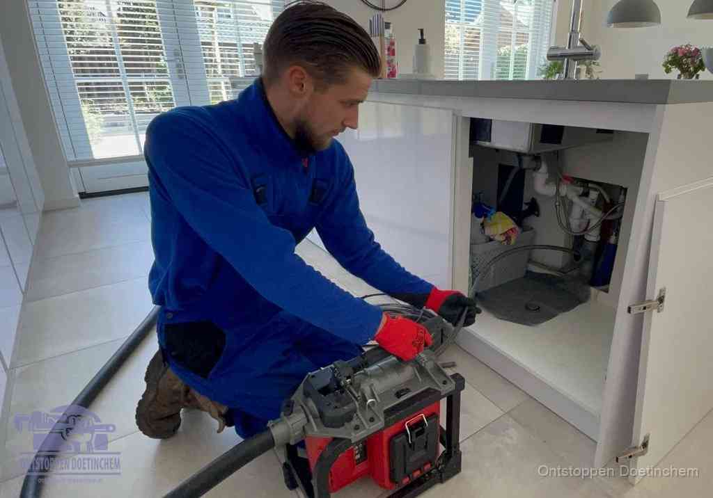 Een monteur voert een professionele elektrische ontstoppingsmachine in de afvoer onder de spoelbak tijdens het gootsteen ontstoppen in Doetinchem