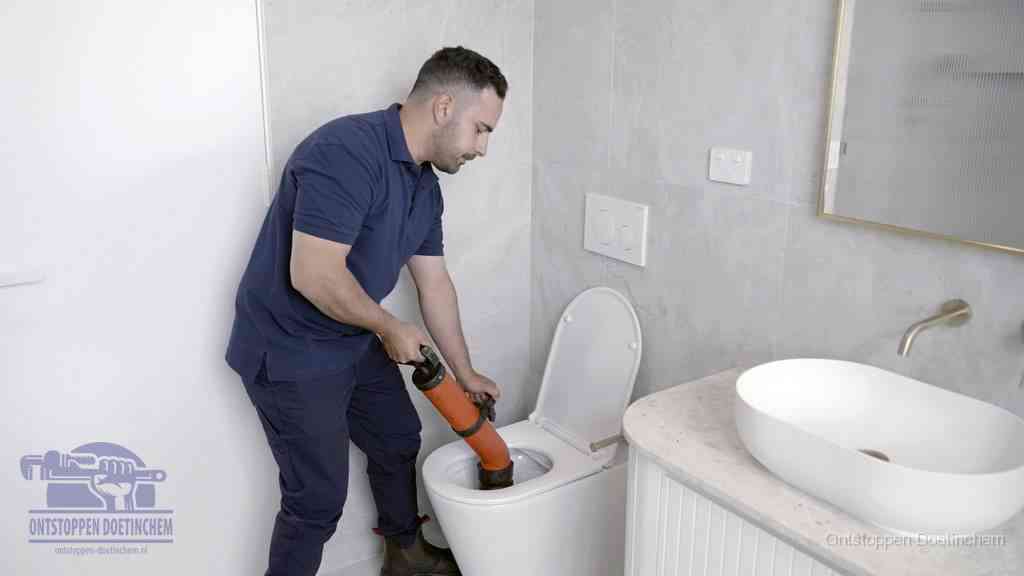 Een man gebruikt een handmatige luchtdruk-ontstopper in een modern betegeld toilet om zelf de wc te ontstoppen in Doetinchem